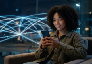 Une jeune femme aux cheveux bouclés souriant devant son smartphone avec un réseau numérique en arrière-plan.