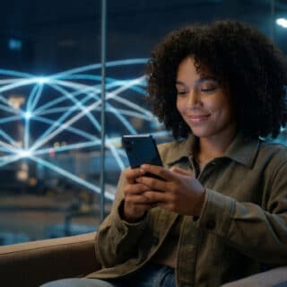 Une jeune femme aux cheveux bouclés souriant devant son smartphone avec un réseau numérique en arrière-plan.