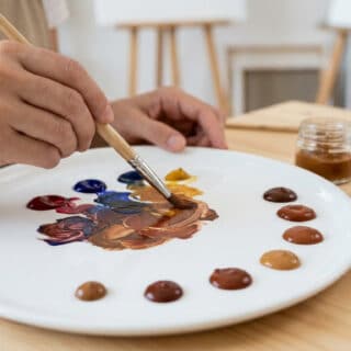 Une main d'artiste mélange des touches de peinture sur une palette en céramique pour créer des nuances de marron.