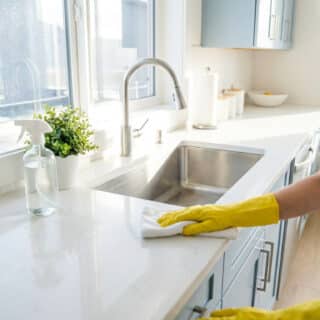 Une femme portant des gants jaunes nettoie un plan de travail blanc dans une cuisine lumineuse.