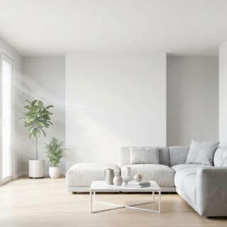 Salon minimaliste blanc avec canapé, grandes baies vitrées laissant passer la lumière et plantes d'intérieur vertes.