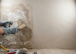 Une personne nettoie un mur humide atteint de salpêtre avec une brosse et un produit de traitement spécialisé.