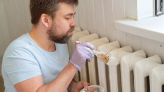 Homme peignant un radiateur blanc au pinceau