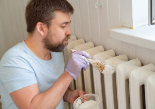 Homme peignant un radiateur blanc au pinceau